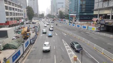 Bu video modern bir şehirdeki hareketli bir sokak sahnesini çekiyor. Kamera, her iki yönde de durmadan hareket eden arabalar ve motosikletler de dahil olmak üzere sürekli trafik dolu geniş bir yolun havadan görüntüsünü sağlıyor.. 