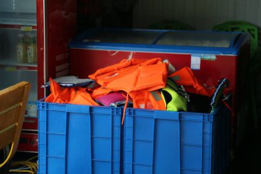 Can yelekleri ve diğer güvenlik ekipmanlarıyla dolu mavi bir plastik kutu, bir dondurma dükkanının açık kapısının yanında, yakın plan çekimlerde yakalanarak ticari bir fotoğrafçılık tarzı yaratılıyor..