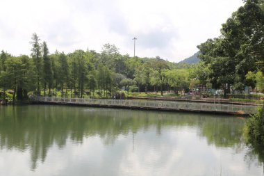 Etrafı yeşil ağaçlarla çevrili küçük bir göl. Kenarlarında demir korkuluklar ve park tarzı yollar var. Önünde başka bir orman alanı daha var. Bazı çocuklar oyun parkı ekipmanlarıyla oynuyor..