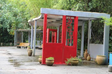 Çin tarzında kırmızı bir kapı, her iki tarafında cam pencereler olan küçük bir pavyon, bambu orman parkının önünde yer alıyor. Saksı bitkilerinin yanında, yeşil ağaçların altında bir ahşap bank duruyor. Kabinin arkasında, beyaz çelik bir bina tepe örtüsü. 