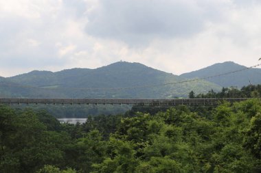Arka planda dağ olan bir nehir üzerinde köprü. Köprü suyun üzerinde asılı.