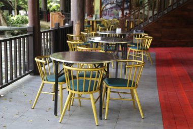 Açık verandada siyah ahşap masaları olan sarı ve yeşil sandalyeler, bir kırmızı halı ve geleneksel Çin tarzı bir açık hava kafesi..