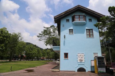 Üzerinde yeşil ve sarı soğutucu olan mavi bir bina. Bina ağaçlar ve otlarla çevrili.