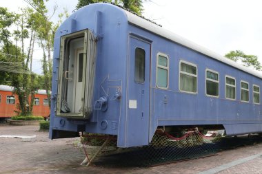Gümüş çatılı ve beyaz panelli eski mavi bir tren vagonu kameraya doğru bir açıda duruyor. Trenin yan taraflarında pencereler var ve ceset açık gri renge boyanmış..