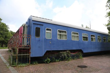 Eski mavi tren vagonu, iki katlı düz bir çatı ve yan kapısı, yan taraflarında beyaz pencereler, her pencerenin bir duvarı kırmızı-pembe renkli, açık havada tuğlalarla çevrili bir alana yerleştirilmiş. Yanında eski balık kurutma makinelerinden yapılmış bir bina daha var.