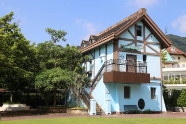 Mavi duvarları ve kahverengi çatısı olan iki katlı küçük bir ev. Pencere ve kapılarında beyaz süslemeler var. Birinci kat açık yeşil renk düzeniyle süslenirken, ikinci katın saçaklarında koyu ahşap aksanlar var..