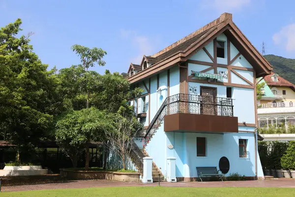 Mavi duvarları ve kahverengi çatısı olan iki katlı küçük bir ev. Pencere ve kapılarında beyaz süslemeler var. Birinci kat açık yeşil renk düzeniyle süslenirken, ikinci katın saçaklarında koyu ahşap aksanlar var..