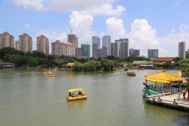 Bir grup küçük tekne bir şehrin önündeki gölde yüzüyor. Teknelerde birkaç kişi var, bazıları da suda.
