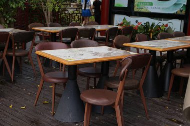 Ahşap zeminde çeşitli masa ve sandalyelerin bulunduğu bir açık hava yemek alanı var. Tablolar, müşterilere gitmeden önce servis edilen yiyeceklerin tozuyla kaplı..