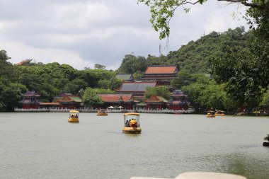 Yazın, bir tarafında eski bir Çin tarzı bina ve önlerinde de birkaç küçük tekne vardır. İnsanlar kürek çekerek ilerlerler. Arkasında yemyeşil ağaçlar ve kırmızı çatılar ve yel de dahil olmak üzere diğer binalar var.