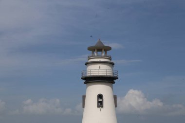 Siyah çatılı uzun beyaz bir deniz feneri. Deniz feneri bulutlu bir günde. Deniz fenerinde uçan kuşlar var.