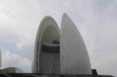 Üst geçitle birbirine bağlı iki uzun, konik yapıya sahip büyük beyaz bir bina. Yapının çatısı kıvrımlı kenarlarla çevrili. Dış duvarlarında geometrik desenler var..