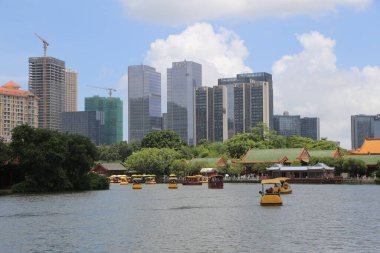 Şehir manzarası yüksek binalar ve şehir parkı gölünün karşısından görülen modern mimari ile gökyüzü manzarası. Su, üzerinde süzülen küçük tekneler gibi sakin. Geleneksel Çin pavyonları ve ağaçları ise kenarlarında süzülüyor..