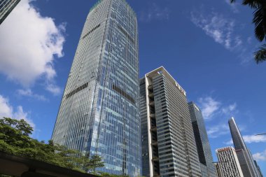 A tall building with a large window is in the middle of a city. There are several other tall buildings in the background