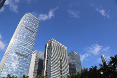 in shenzhen, the city's modern buildings stand tall against the blue sky and white clouds. the high-rise office building stands gracefully in front of them, adorned with glass curtain walls that reflect the sunlight