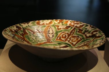 a ceramic bowl with medieval italian decorative motifs, featuring a green and brown glaze, displayed in a museum setting with appropriate lighting