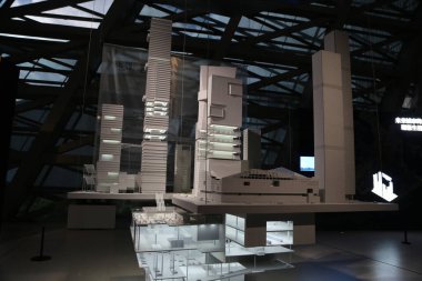 a white model of tall buildings, a glass building display on the left side with two floors and three floors, white models placed in a large space with a black background wall