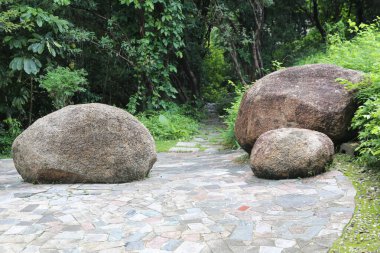 three large stone boulders on the right and left sides of an outdoor cobblestone pathway, surrounded by lush greenery in the forest park