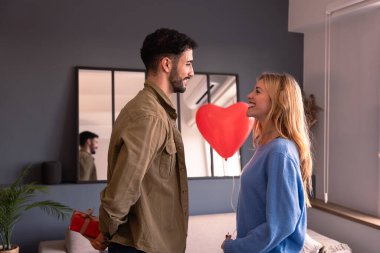 Sevgilisine sürpriz bir Sevgililer Günü hediyesi veren erkek arkadaşı elinde kalp şeklinde bir balon tutuyor..