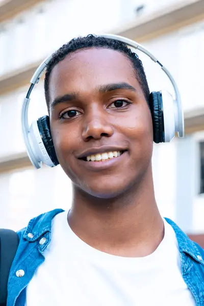 ヘッドフォン付き大学で屋外に立っている若い黒人男性の学生 ライフコンセプトを学ぶ — ストック写真