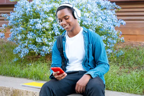 Szczęśliwy Student Słuchawkami Folderem Jest Kampusie Uniwersyteckim Używając Aplikacji Mediach — Zdjęcie stockowe