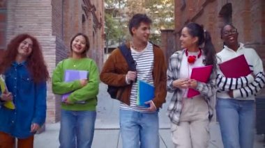 Çok ırklı bir grup öğrenci üniversitede yürüyor, dışarıda gülüyor. Gençler birlikte eğleniyor..