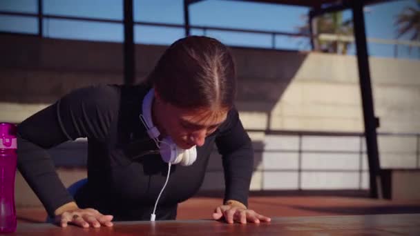スポーツヘッドフォン付き集中女性が床にスポーツウォーターボトルでプッシュアップ — ストック動画