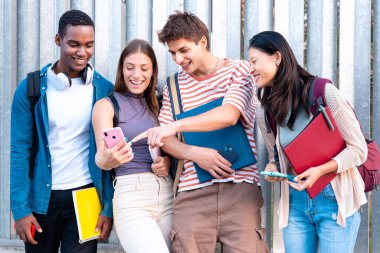 Genç adam sınıf arkadaşlarına komik bir şey doğrultuyor. Akıllı telefon ekranında, diğer arkadaşlarıyla gülüyor. Kampüs konsepti: Üniversite hayatı