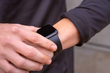 Açık havada akıllı bir saate bakan genç bir sporcunun kısmi görüntüsü..