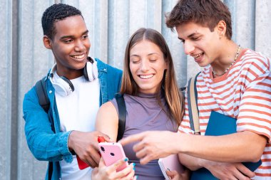 Gülümseyen genç bir çocuk cep telefonu ekranında arkadaşlarına komik bir şey gösteriyor..