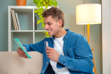 Kanepede oturan genç yetişkinler kolay ve güvenli elektronik ödemeleri yapabilmek için kredi kartı numaralarını tablete yazmaktan mutlu olurlar.