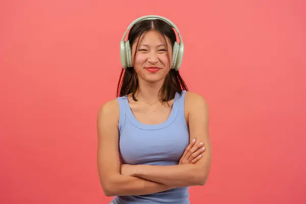 Szczęśliwa Chińska Kobieta Słuchawkami Różowym Tle Ramionami Skrzyżowanymi Patrząc Kamerę — Zdjęcie stockowe