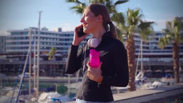 Χαρούμενα Σπορ Κορίτσι Ένα Τηλεφώνημα Κρατώντας Ένα Αθλητικό Μπουκάλι — Αρχείο Βίντεο