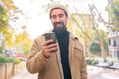  Mutlu bir adamın portresi cep telefonuna bakıyor, gülümsüyor, bir uygulama kullanarak mesaj yolluyor. İnsan duyguları kavramı, yüz ifadesi. 