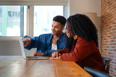 Gülümseyen genç, çok kültürlü bir çift evdeki masada dizüstü bilgisayarlarıyla cihazda kablosuz internet taraması yapıyor. Çok ırklı bir erkek ve kadın dizüstü bilgisayarla internette gezinirken eğleniyor..