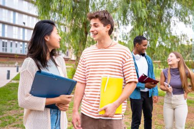  Çok ırklı üniversite ödevleri ve üniversite kampüsünde yürüyüş yaparak öğrenme dersi. Üniversite hayatı kavramı. Dört mutlu genç öğrencinin üniversite notlarıyla konuşması.. 