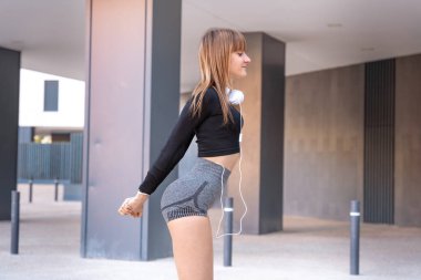 Spor kulaklık takan, spor kulaklık takan, sırıtan, açık havada kameraya bakan genç bir kadın..