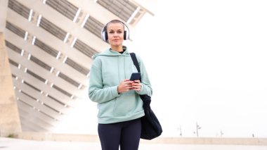 Egzersiz yapmaktan yorgun kulaklıklı atletik bir kadın kameraya bakan bir cep telefonu mesaj uygulamasını kullanmak için ara veriyor..