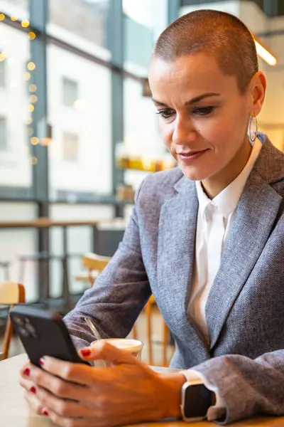 Satisfied with the results, the businesswoman who takes a break in a cafe looks at the results with satisfaction. A mature boss holds a phone in her hands, writes messages online, using an app.