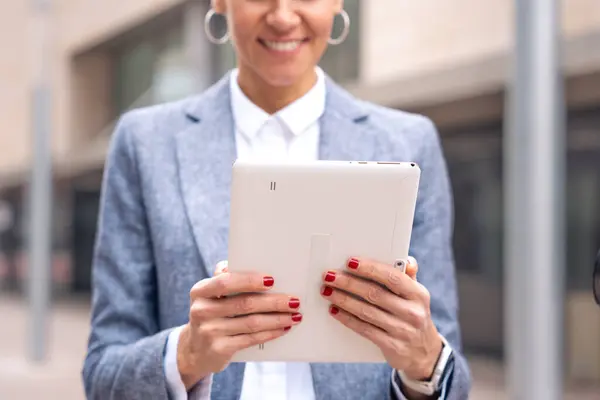 Ofis binasının önünde yürüyen iş kadınının sonuçlarına sahip düşünceli bir iş kadını, olgun bir patron elinde bir telefon tutuyor, bir uygulama kullanarak mesajlar yazıyor ve internetten haberleri okuyor..