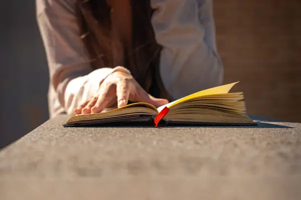 Konsantre olmuş beyaz kadın kitap okuyor, yüzüstü yere oturuyor..