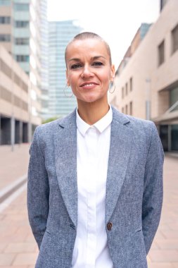 Beyaz bir iş kadınının dış mekanda duran takım elbisesiyle kameraya gülümseyen görüntüsü. Düşünceli bir ifadeyle genç bir avukatın bakışları.