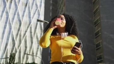 Üniversite kampüsünde kahve içerken cep telefonuyla konuşan gözlüklü genç siyahi kız öğrenci. Kavram: Üniversite hayatı