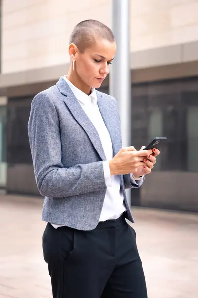 Satisfied with the results, the businesswoman walking on the street outside the office building, a mature boss holds a phone in her hands, writes messages and reads news online, using an app.