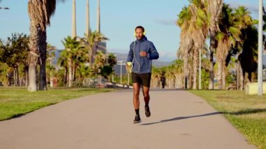  Kulaklık takan genç koşucu elinde soğuk izotonik spor suyu tutuyor..