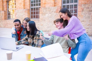 Laptopları ve akıllı telefonları olan beş öğrenci sınavı incelemek için kampüsün yakınında oturuyor. Bilgisayarlı öğrenciler kampüsün yanında oturup iletişim kuruyorlar..