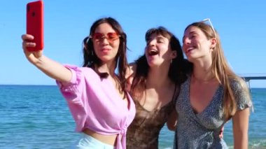 Bir grup gülümseyen, etnik çeşitlilikte kadın tatilde. Neslin güzel ve neşeli kızları cep telefonlu bir fotoğraf için poz verir..