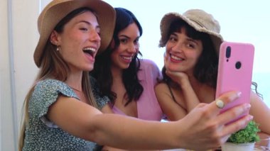 Mayo giymiş, gülümseyen, etnik çeşitliliğe sahip bir grup kadın tatilin tadını çıkarıyor. Z neslinin güzel ve neşeli kızları cep telefonlu bir fotoğraf için poz veriyor..