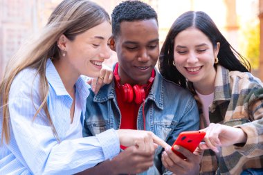 Bir grup arkadaş, kampüste cep telefonuyla internette gezinen akıllı telefonlarına bakıp işaret ediyor.