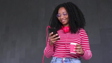 Kıvırcık saçlı güzel siyahi kadın arkadaşlarıyla sohbet etmek için akıllı telefonunu kullanıyor. bağlı kavram açık havada